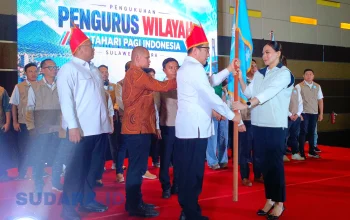 Ketum PB MPI, Dr. Sutia Budi, menyerahkan panji pataka kepada Ketua PW MPI Sulawesi Utara, Theresia Inggrid Manangka, dalam prosesi pengukuhan di Manado, Jumat (30/10/2026). Panji organisasi resmi dikibarkan untuk membumikan gerakan sosial dan kebudayaan di Bumi Nyiur Melambai. (Foto: Ridho L Tobing)